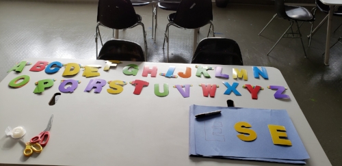 Gray work table with stencils, scissors, construction paper, sharpie. The stencils are organized alphabetically at the top of the table, the other supplies at the bottom.