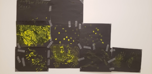 Picture of stars &amp; constellations from a poetry workshop. Black construction paper taped together with yellow finger paint on them. To the left are two columns of three, then a column of two, then one all the way on the right. The finger painting is different in each, some dots, some swirls and some full hand prints are visible.