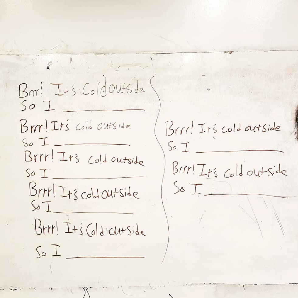 Words on a white board in black expo marker read “Brrr! It’s cold outside / so I” with a long line after “I” for student response.